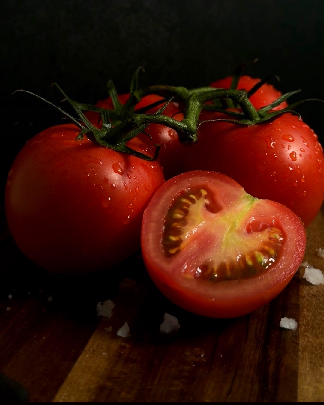 Fresh red tomatoes with water droplets and sea salt on a dark wooden board